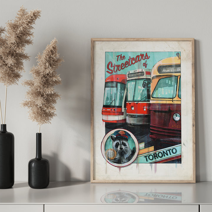 Streetcars of Toronto Poster by Rob Croxford in wooden frame sitting on a drawer with black mantel bottle next to it. 