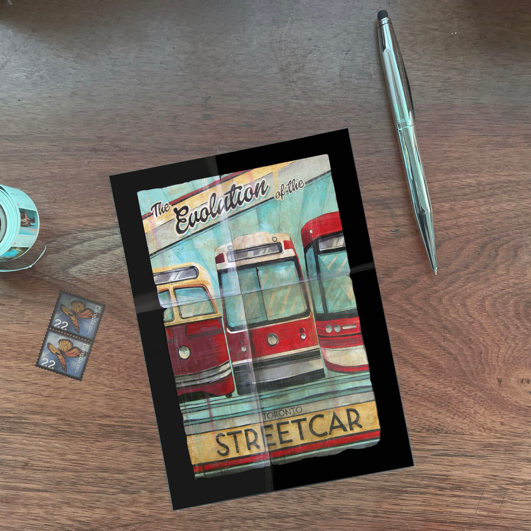 Three Toronto Streetcars Postcard by Rob Croxford on a desk with a pen and stamps