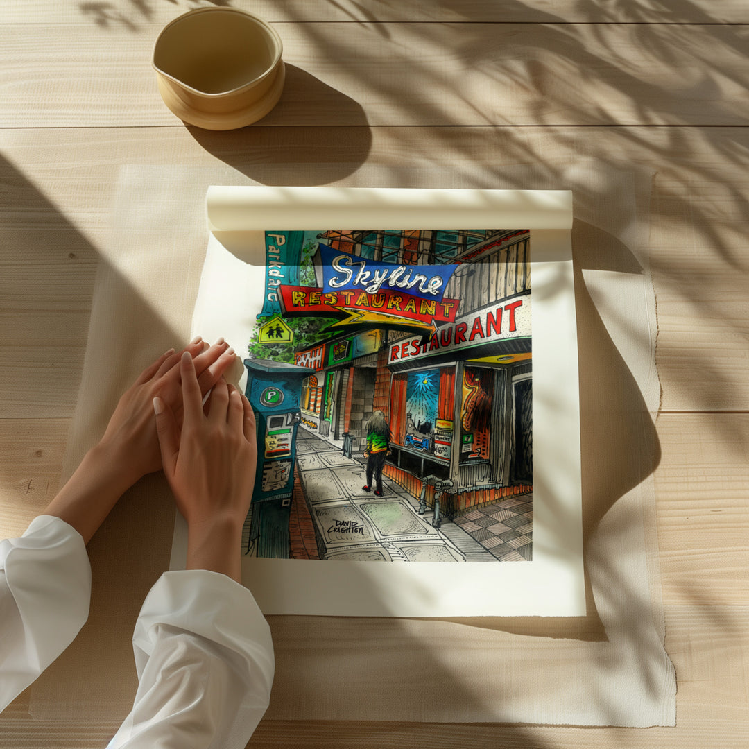Beautiful illustration of Skyline Restaurant from Toronto Art Shop on a wooden desk, dappled in sunlight. 