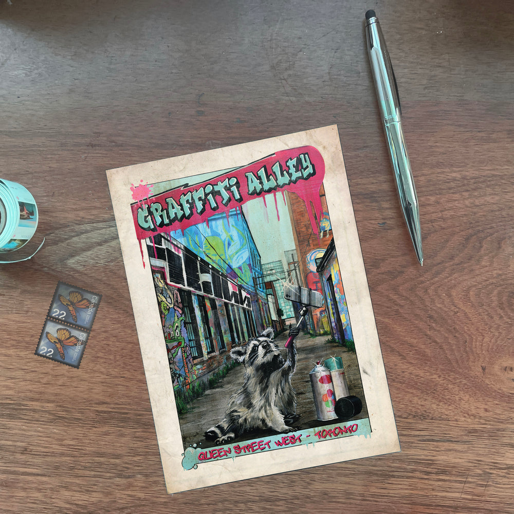 Raccoon Graffiti Alley Toronto Postcard on Mahogony Desk with pen and stamps
